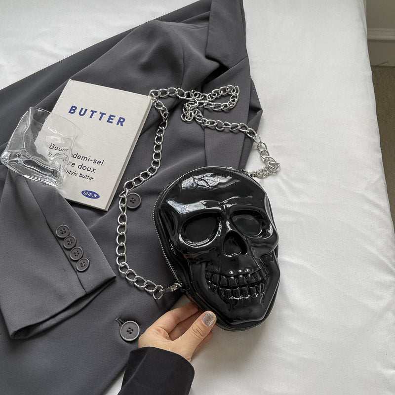 Black silicone women's fashion chain bag shaped like a skull with a silver chain strap on a gray blazer