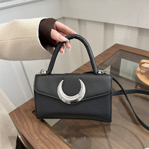 Black retro fashion shoulder bag with crescent moon clasp and single handle on wooden table