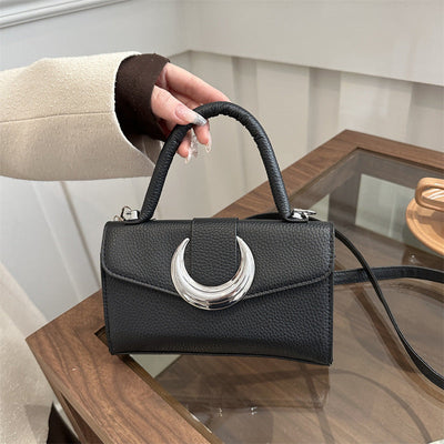 Black retro fashion shoulder bag with crescent moon clasp and single handle on wooden table