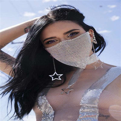 Woman wearing rhinestone metal jewelry mask and star-shaped earrings against blue sky