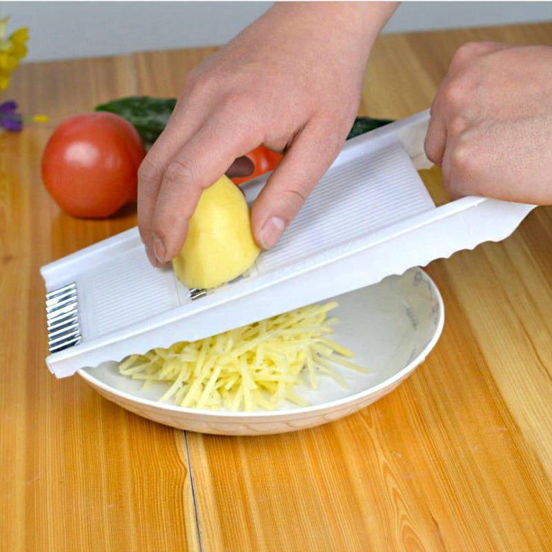 Home kitchen multifunctional grater shredding potato into thin strips over a bowl on wooden table