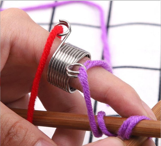 Metal wire guide knitting gadget wrapped around fingers holding purple and red yarn on wooden knitting needle