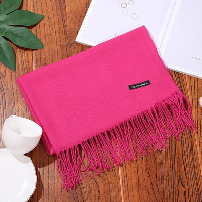 Pink cashmere women scarf shawl with fringed edges on wooden surface