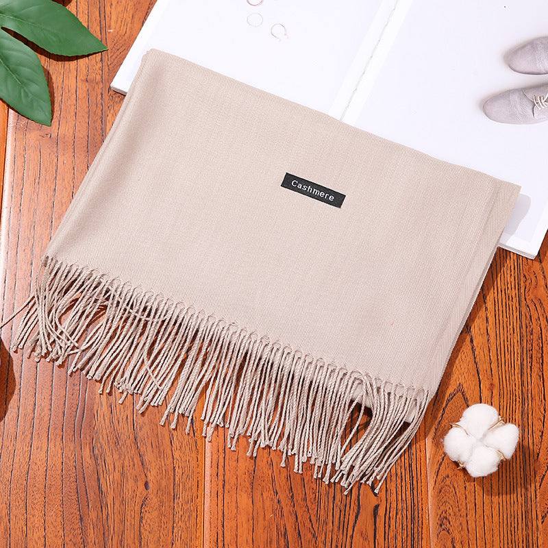 Beige cashmere women scarf shawl with fringes on wooden surface next to cotton flower and book