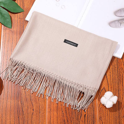 Beige cashmere women scarf shawl with fringes on wooden surface next to cotton flower and book
