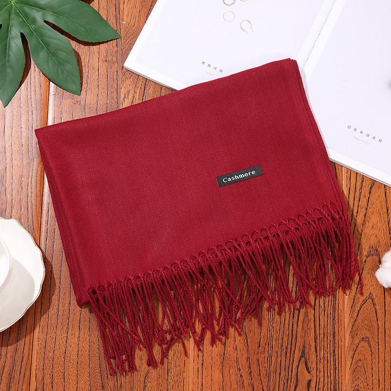 Red cashmere women scarf shawl with fringe detail on wooden surface with leaves and white cup