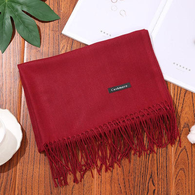 Red cashmere women scarf shawl with fringe detail on wooden surface with leaves and white cup