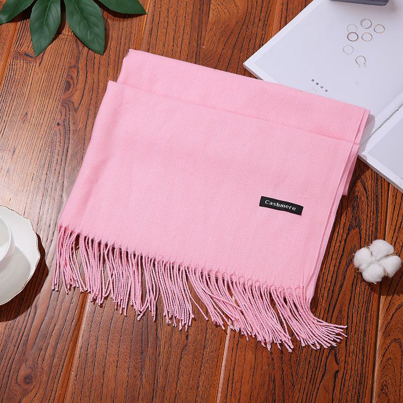 Pink cashmere women scarf shawl with fringe on wooden surface next to jewelry and cotton decor