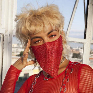 Person wearing red rhinestone metal jewelry mask and matching red fishnet top with chain details outdoors