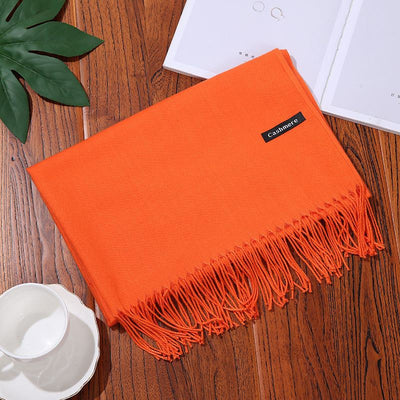 Orange cashmere women scarf shawl with fringe on wooden table with white teacup and green leaf decoration