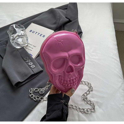 Pink silicone skull-shaped women's fashion chain bag with silver chain strap on gray jacket background