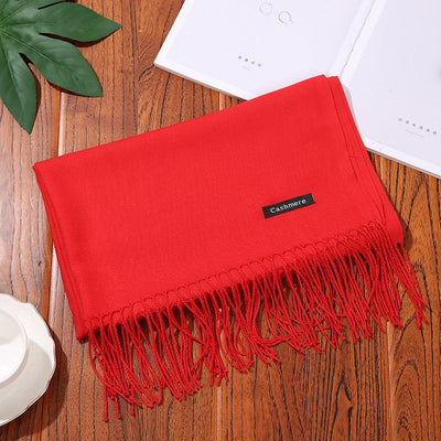 Red cashmere women scarf shawl with fringed edges on wooden surface