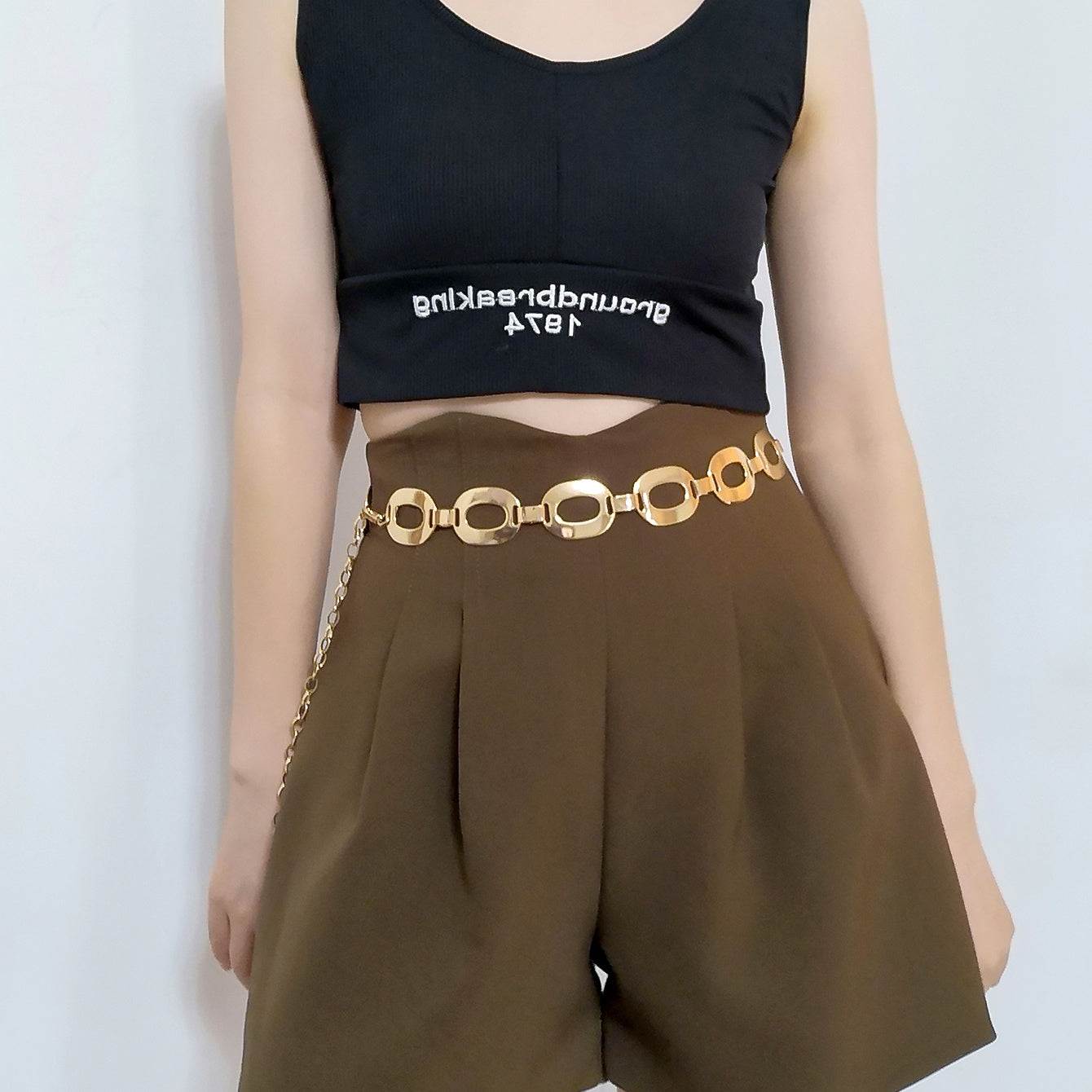 Gold metal summer jewelry waist chain with hollow-out design worn with high-waist brown shorts and black crop top