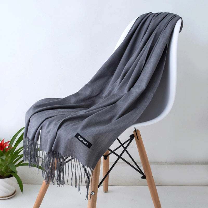 Soft grey cashmere women scarf shawl with fringed edges draped on a modern white chair