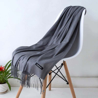 Soft grey cashmere women scarf shawl with fringed edges draped on a modern white chair