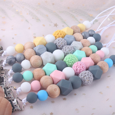 Colorful baby silicone pacifier chains with wooden and silicone beads and clips on light fabric background