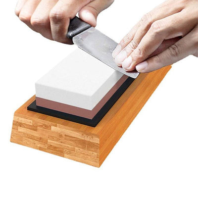 Hand sharpening a kitchen knife on a double-sided home kitchen whetstone with bamboo base