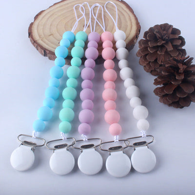 Colorful silicone bead baby pacifier clips with metal clasps arranged on white surface next to pinecones and wooden slice