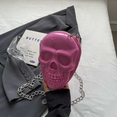 Pink silicone women's fashion chain bag shaped like a skull with a silver chain strap held over gray blazer background