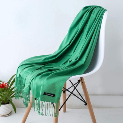 Green cashmere women's scarf shawl with fringe draped over white chair, soft and skin-friendly autumn winter wrap