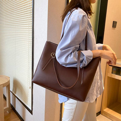 Trendy brown PU leather handbag with simple design worn by woman in casual outfit